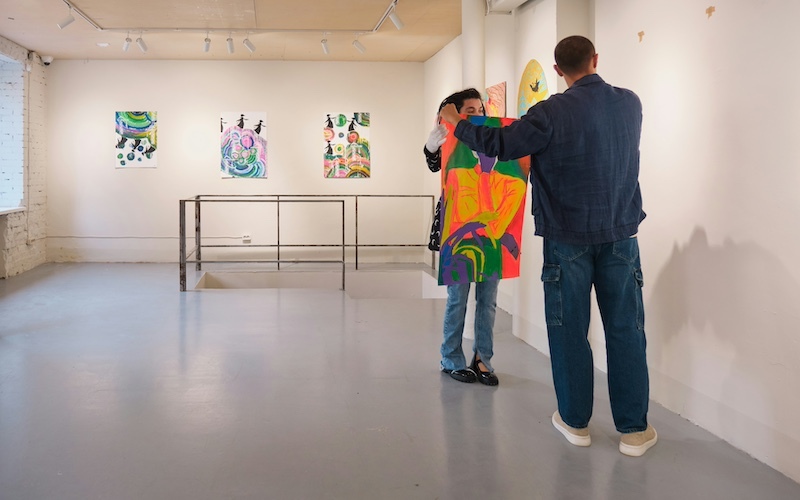 Two people holding onto an abstract painting on paper in a white gallery with abstract artworks on the wall